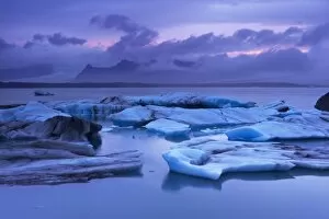 Icebergs in Jokulsarlon glacial lagoon, at dusk, Oraefajokull (Vatnajokull) glacier in the distance