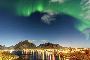 Reine Prints: Illuminated harbor of Reine reflected in the cold arctic sea during the Aurora Borealis (Northern Lights)