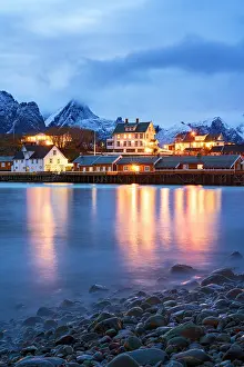 Sakrisoy Prints: Illuminated rorbu and mountains reflect in the sea at dusk in Sakrisoy