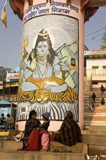Indian people go about their daily business in front of a pillar painted with the Hindu god Shiva on that ghats of