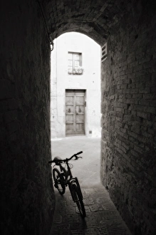 Bicycles Prints: Infra red image of a bicycle in shady alleyway, San Quirico d Orcia