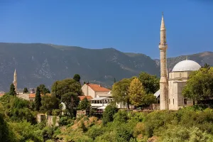 Mostar Prints: Koski Mehmed Pasha Mosque stands tall in Mostar with Dinaric Alps in the background under bright blue sky