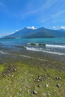 Swimming Prints: Lakeshore view of beach in Dongo by Lake Como with clear sky and distant mountains in Italy