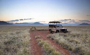 Barren Prints: Land rover game vehicle parked by sand road at sunrise