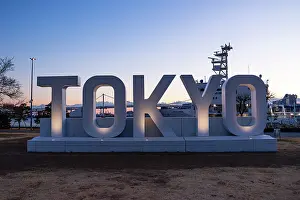 Tokyo Prints: Large illuminated TOKYO sign at sunset with Rainbow Bridge and city skyline in the background at Odaiba Seaside Park