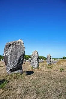 Stones Prints: Large stones stand in a field under a clear blue sky in France with grass surrounding the ancient site during daylight