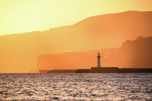 Glow Prints: A lighthouse stands against golden coastal cliffs in AlmerAa