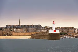 Navigation Prints: Lighthouse and stone jetty mark entrance of harbor with view of town in Brittany, France