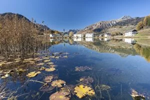 The little village of Tarasp in Low Engadine reflecting in a nearby pond, half covered in water lily leaves, Graubunden