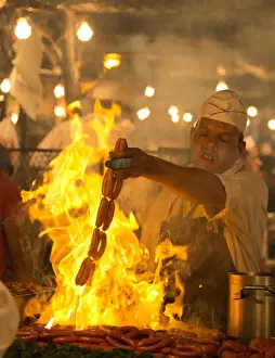 Subsistence Prints: Local man cooking sausages on open flame at one of the food stalls in the Djemaa el Fna