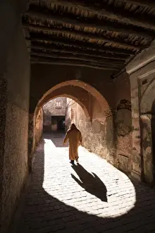 Typically Moroccan Prints: Local man dressed in traditional djellaba walking through archway in a street in the Kasbah