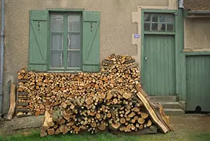 Fuel Prints: Logs piled outside a traditional cottage with shutters at the window, at Meuse