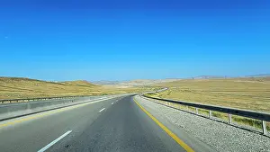 Northern Prints: Long and winding road stretches through arid landscape in Northern Azerbaijan under clear blue sky
