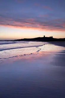 Embleton Prints: Looking across Embleton Bay at sunrise towards the silhouetted ruins of Dunstanburgh Castle in the distance