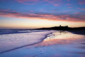 Forts Prints: Looking across Embleton Bay at sunrise towards the silhouetted ruins of Dunstanburgh Castle in the distance