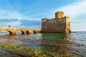 Mature Man Prints: Man on the bridge walks to the fortified castle of Torre Astura in the water of Tyrrhenian Sea built on ruins of Roman