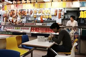 Man in cafe with hanging roast duck and pork and Chinese menus, Hong Kong, China, Asia