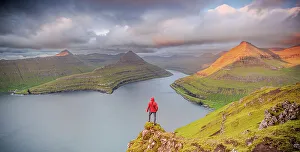 Mid Adults Prints: One man contemplating the sky at dawn standing on rocks above a fjord