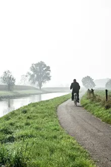 North Brabant Prints: Man cycling on countryside cycle path next to the River Mark in autumn
