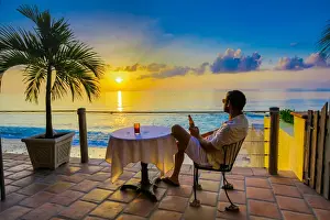 40 45 Years Prints: Man enjoying a beverage on a patio at sunset in Turks and Caicos Islands, Atlantic