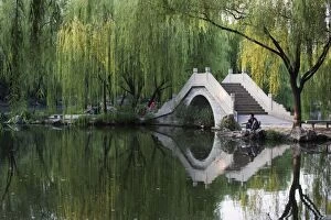 Man fishing next to a stone arched bridge in Zizhuyuan Black Bamboo Park