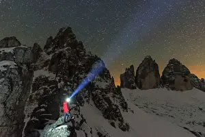 One Mature Man Only Prints: Man with head torch illuminates the starry sky over the snowy Paterno mountain and Tre Cime di Lavaredo (Lavaredo peaks)