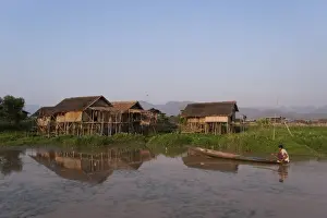 Stilt House Prints: A man paddles his canoe past one of the floating villages on Inle Lake, Myanmar (Burma)