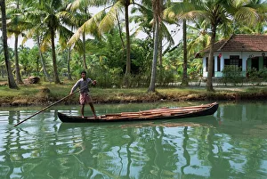 Kerala Prints: Man with pole pushing boat forwards on a Kerala backwater