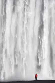 Man in red jacket standing in front of the 62m high Skogafoss waterfall near the village of Skogar