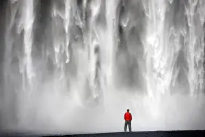 Skogar Prints: Man in red jacket standing in front of the 62m high Skogafoss waterfall near the village of Skogar