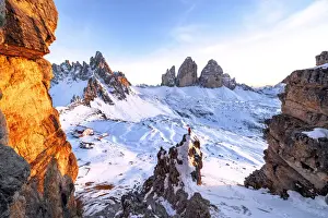 Man on rocks admiring the snowy Monte Paterno and Tre Cime di Lavaredo at sunset