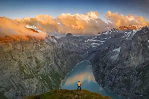 Man standing on rocks looking at clouds at sunset over lake Limmernsee, aerial view