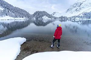 Search Results: Man standing on shores of Lake Cavloc admiring the snowy woods, Bregaglia Valley