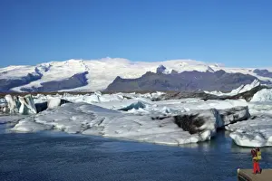 Jokulsarlon Prints: Man taking photo of icebergs on the glacial lake at Jokulsarlon with snow on the massive icecap of Vatnajokull behind