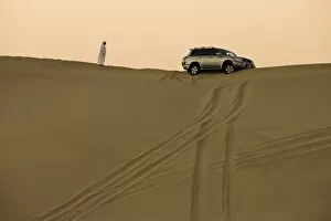Images Dated 30th October 2008: Man in traditional Arab dress looking at 4x4 car stuck on the ridge of a dune during a desert