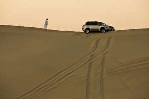 Images Dated 30th October 2008: Man in traditional Arab dress looking at 4x4 car stuck on the ridge of a dune during a desert