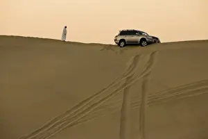 Descend Prints: Man in traditional Arab dress looking at 4x4 car stuck on the ridge of a dune during a desert safari near Abu Dhabi
