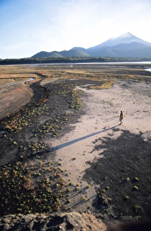 Man walking on dry lake bed with Llaima Volcano in distance, Conguillio National Park Man walking on dry lake bed with Llaima Volcano in distance, Conguillio National Park