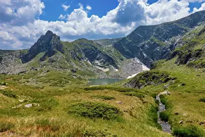 Hilltops Prints: Meadow and stream flow under peaks with a lake in the distance in the Rila Mountains of Bulgaria