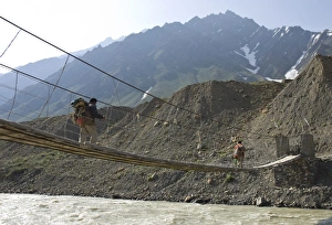 Two men carrying backpacks crossing a wooden suspended