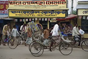 Rick Shaw Prints: Men riding cycle rickshaws on the street passing the outside of a hotel