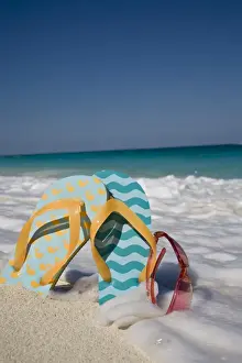 Objects Prints: Two mismatched beach flip-flops with red sunglasses in the surf on a Caribbean beach