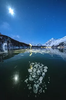 Search Results: Full moon on ice skater on frozen Lake Sils lit by head torch, Engadine