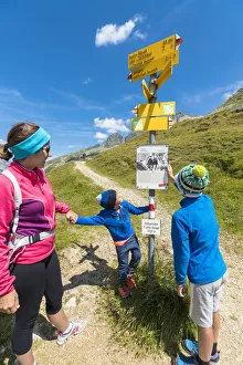 Mother and sons look at the signpost of hiking trails, Spluga Pass, Chiavenna Valley