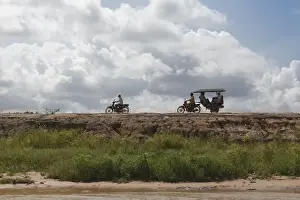 Rick Shaw Prints: A motorbike being followed by a moto-rickshaw along the banks of the Tonle Sap Lake