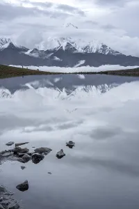 Trail Prints: Mount Gongga rises above clouds with Lenggacuo Lake reflecting Daxue Mountain Range in Sichuan