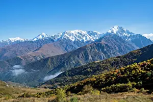 Bright Prints: Mountain scenery in North Ossetia with snow-capped peaks and colorful autumn trees under clear blue sky