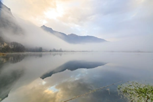 Mountains reflected in water at dawn shrouded by mist, Pozzo di Riva Novate, Mezzola