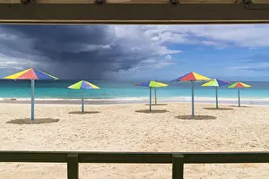 Antigua Prints: Multicolored striped umbrellas on white sand beach under storm clouds