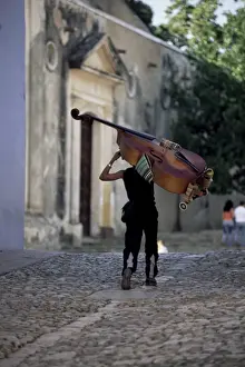 Carrying Prints: Musician carrying double bass along cobbled street to Plaza Mayor, Trinidad